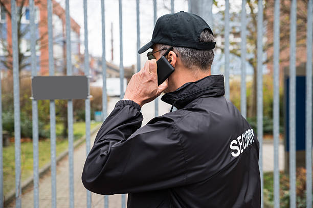 Confident mature security guard talking on mobile phone in front of gate