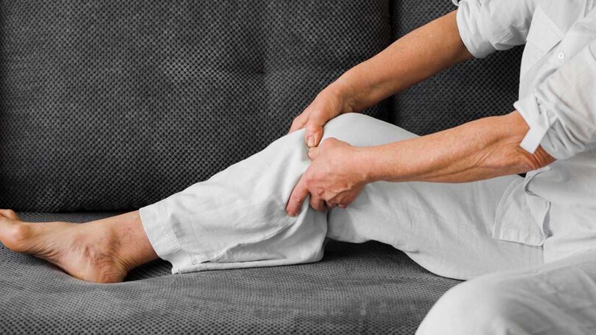 A person seated on a couch, visibly distressed, holding their leg in pain, indicating discomfort and seeking relief.