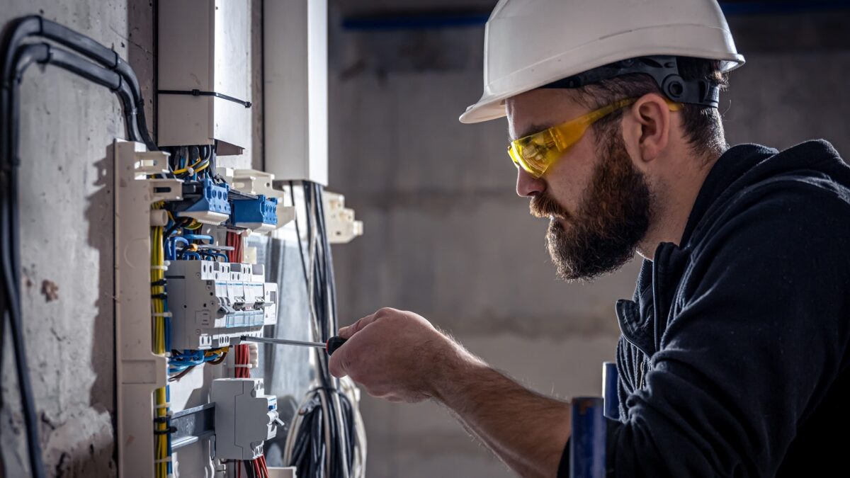 A male electrician works in a switchboard with an electrical connecting cable.