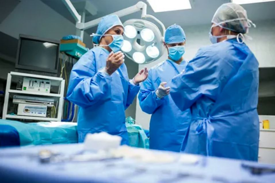 Surgeons performing a procedure in a sterile operating room, focused on their tasks with medical equipment surrounding them.