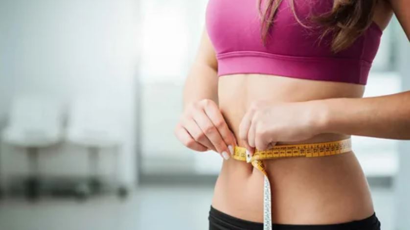 A woman measuring her waist with a tape measure, focusing on her health and fitness goals.