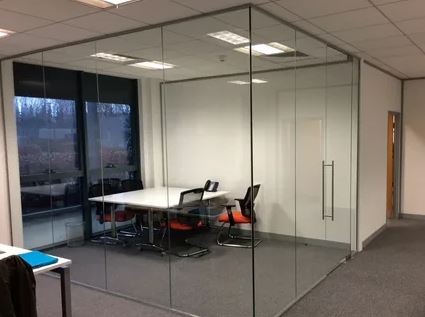 A modern office featuring a glass partition, equipped with a table and chairs for collaborative work.