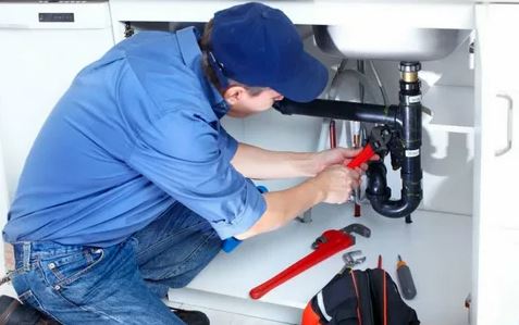 A plumber repairs a kitchen sink, tools in hand, ensuring proper functionality and maintenance of the plumbing system.